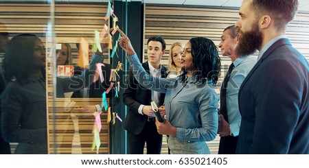 Creative group of business people brainstorming putting sticky notes on glass wall in office