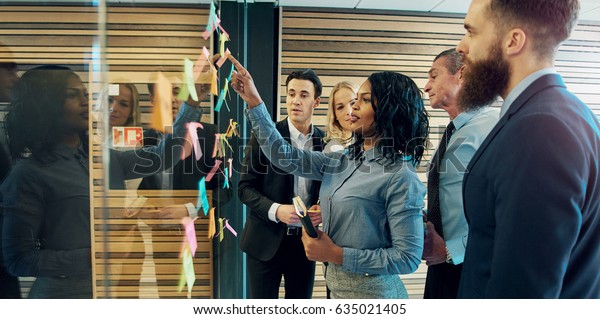 Creative group of business people\
brainstorming putting sticky notes on glass wall in\
office