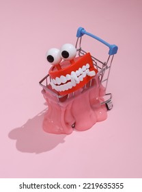 Creative Halloween Layout, Mini Shopping Trolley With Slime And Monster Jaw On Pink Background With Shadow. Visual Autumn Trend. Fresh Idea. Concept Pop. Trick Or Treat