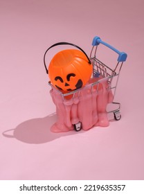 Creative Halloween Layout, Mini Shopping Trolley With Slime And Bucket On Pink Background With Shadow. Visual Autumn Trend. Fresh Idea. Concept Pop. Trick Or Treat