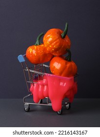 Creative Halloween Layout, Shopping Trolley With Neon Slime And Pumpkins On Two Tone Dark Background. Visual Trend. Trick Or Treat