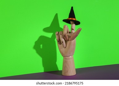 Creative Halloween Still Life. Puppet Hand Holding Witch Hat On Green Purple Background