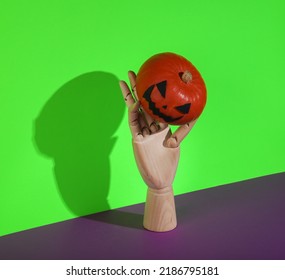 Creative Halloween Still Life. Puppet Hand Holding Halloween Pumpkin On Green Purple Background