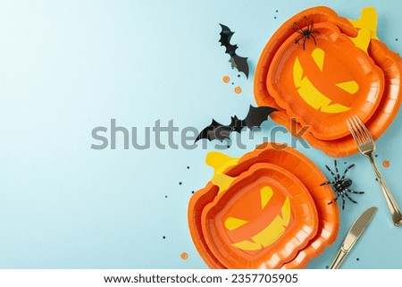 Creative Halloween table decor from top view. Jack-o'-lantern-shaped plates, cutlery, creepy crawlies, bats, and confetti on soft blue surface, space for text