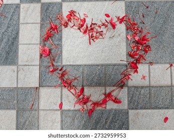 Creative heart shape formed using fallen pink flowers on an outdoor patterned tile floor, representing love and affection.