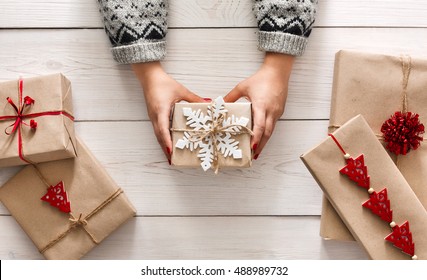 Creative Hobby. Woman's Hands Show Christmas Holiday Handmade Present In Craft Paper With Twine Ribbon. Holding Xmas Gift Box, Decorated With Snowflake, On White Wooden Table Background, Top View.