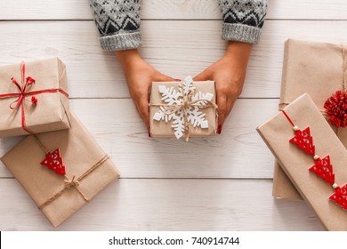 Creative Hobby. Woman's Hands Show Christmas Holiday Handmade Present In Craft Paper With Twine Ribbon. Holding Xmas Gift Box, Decorated With Snowflake, On White Wooden Table Background, Top View.