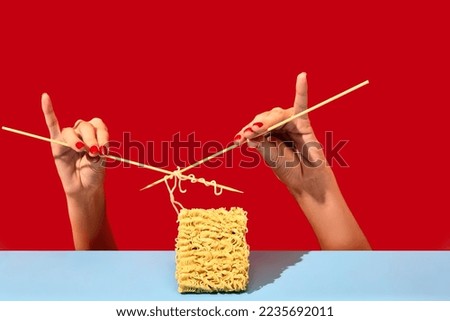 Creative image with female hands knitting instant noodles on blue table over vivid red background. Dinner. Food pop art photography. Creativity. Complementary colors. Copy space for ad, text