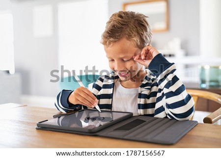 Creative kid drawing on tablet using digital pen. Child using pen on tablet to draw and complete homework. Cute little boy using stylus on screen and drawing pictures at home.