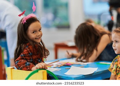Creative kids during an art class in a daycare center or elementary school classroom drawing with female teacher.