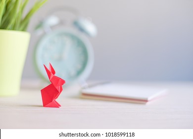 Creative lay out.Red rabbit paper origami with blur alarm clock, green tree and note book in background.rabbit origami with copy space.Selective Focus shot.
