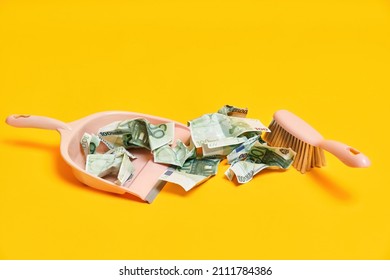 Creative layout with dustpan, hand brooms and crumpled money dollar bills on yellow background. Finance, corruption, criminal activity concept