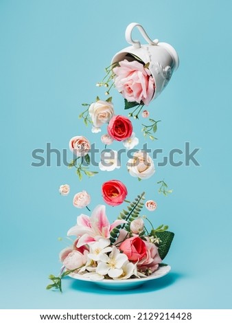 Creative layout with fresh flowers and leaves flying and pouring from tea cup on pastel blue background. Creative floral spring bloom concept. Still life natural visual trend.