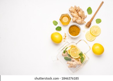 Creative layout made of clear glass teapot with ingredients. Hot seasonal tea against viruses. Ginger, turmeric, honey and lemon  ingredients. Immune system support with alternative medicine