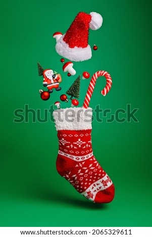 Creative layout made with flying Christmas socks, Santa Claus, pine tree and candy cane on green background. Minimal New Year season concept. Winter holidays idea.