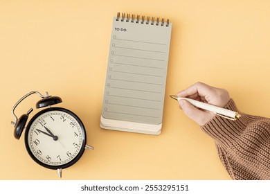 Creative layout made with woman's hand holding white pen, To do list in spiral notepad and retro alarm clock. Trendy pastel background, flat lay style. Planning concept. - Powered by Shutterstock