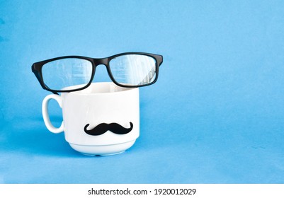 Creative layout on Happy Fathers Day with funny face from cup of coffee, eyeglasses and tie mustache on blue background. Copy space. Greeting card for daddy. - Powered by Shutterstock