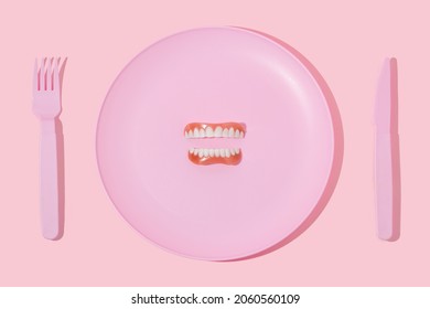 Creative layout with pastel pink plate, fork,knife and false or fake teeth on pastel pink background. Minimal surreal breakfast idea or food restaurant concept. Aesthetic 80s or 90s fashion idea.