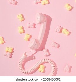 Creative layout with pink retro telephone handset and pink and yellow gummy bears on pastel pink background. Retro fashion aesthetic idea with phone. Minimal romantic communication concept.