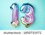 Creative layout. Rainbow foil balloon number, digit thirteen. Birthday greeting card with inscription 13. Anniversary concept. Top view. Stylish colored numeral on blue background. Numerical digit.