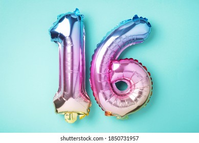 Creative layout. Rainbow foil balloon number, digit sixteen. Birthday greeting card with inscription 16. Anniversary concept. Top view. Stylish colored numeral on blue background. Numerical digit.