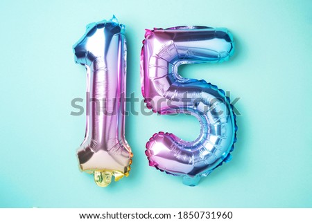 Creative layout. Rainbow foil balloon number, digit fifteen. Birthday greeting card with inscription 15. Anniversary concept. Top view. Stylish colored numeral on blue background. Numerical digit.