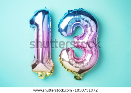 Creative layout. Rainbow foil balloon number, digit thirteen. Birthday greeting card with inscription 13. Anniversary concept. Top view. Stylish colored numeral on blue background. Numerical digit.