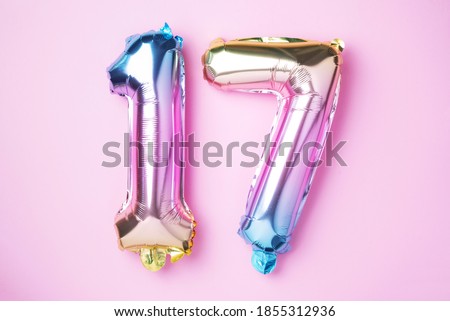 Creative layout. Rainbow foil balloon number, digit seventeen. Birthday greeting card with inscription 17. Anniversary concept. Top view. Stylish colored numeral on pink background. Numerical digit.