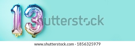 Creative layout. Rainbow foil balloon number, digit thirteen. Birthday greeting card with inscription 13. Anniversary concept. Top view. Stylish colored numeral on blue background. Numerical digit.