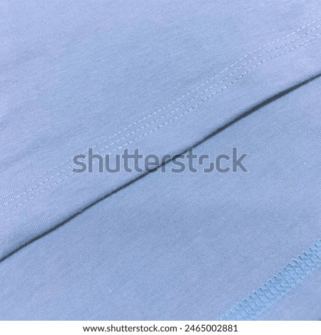 creative layout of sky blue plain basic t-shirt cotton material with stitching details zoom. flat lay, fashion and textile background