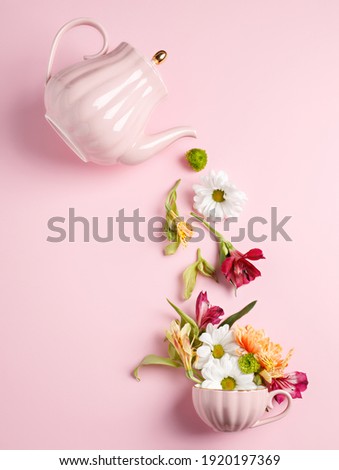 Creative layout with tea pot pouring fresh flowers and leaves into tea cup on pastel pink background. Creative floral spring bloom concept. Still life visual trend. Flat lay.