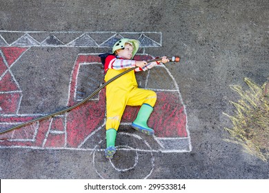 Creative leisure for kids: Little kid boy of four years having fun with fire truck picture drawing with chalk, outdoors. Dreaming of future profession.