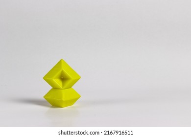Creative light yellow designed plastic geometrical sculpture against pastel white background with shadows.