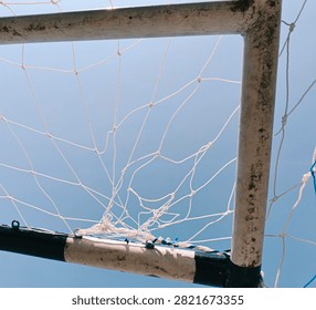 A creative low-angle photograph looking up at the corner frame of a soccer goal post and white mesh net set against a clear blue sky.
