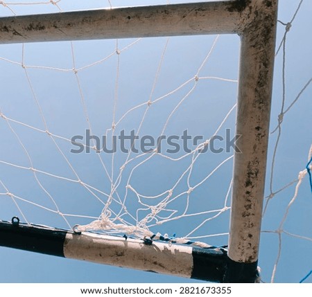 A creative low-angle photograph looking up at the corner frame of a soccer goal post and white mesh net set against a clear blue sky.