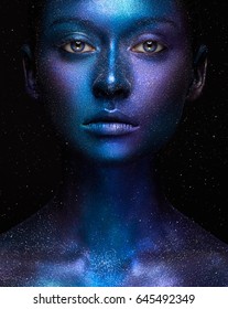 Creative make-up and beauty theme: beautiful girl model with cosmic make-up on face and body blue and purple skin color on dark background in studio