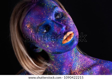 Creative make-up and beauty theme: beautiful girl model with cosmic make-up on her face blue skin color with colorful paints paints on a dark background in the studio