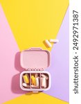 Creative medical and health care composition: open pill box with white and yellow capsules on colourful background. Daily medication and supplement management, health and wellness concept.