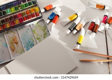 Creative mess in the artistic workshop. Empty copy space canvas, acrylic paints in tubes, brushes, pencils, pastels, palette knife. Top view.
