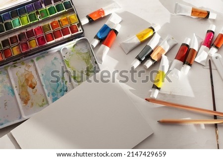 Creative mess in the artistic workshop. Empty copy space canvas, acrylic paints in tubes, brushes, pencils, pastels, palette knife. Top view.