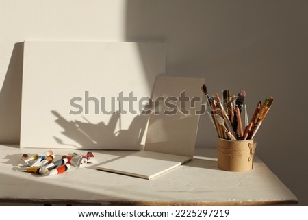 Creative mess in the artistic workshop. Empty copy space canvas, acrylic paints in tubes, brushes, pencils, pastels, palette knife. 