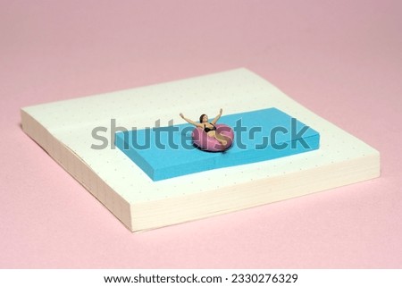 Creative miniature people toy figure photography. Sticky notes installation. A girl on a rubber tube boat chilling at swimming pool. Image photo