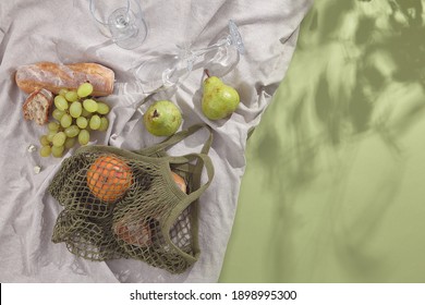 Creative Minimal Summer Picnic Flat Lay. Reausable Bag With Fruit And Textile Cloth On Green Background. Spring Eco Friendly Picnic. Creative Reusable Lifestyle