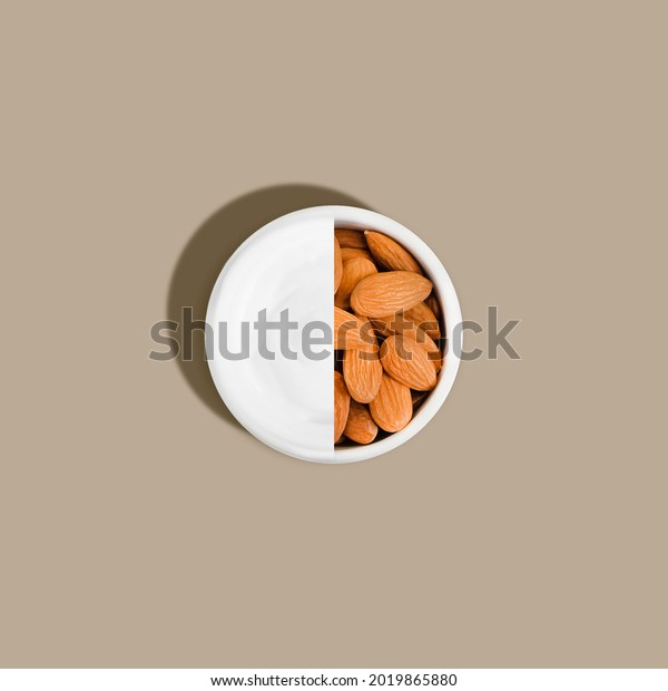 Creative mockup with almonds and cream in a round\
white jar on a beige background with hard shadow and light. Organic\
cosmetic product made from natural ingredients for face and body\
skin care.