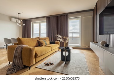 Creative and modern vintage living room interior design with yellow sofa, coffe table, lamella wall with tv. Herringbone parquet with chest of drawers, brown curtain in windows. Template. 