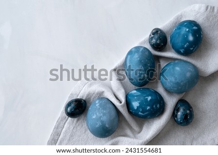 Creative naturally dyed blue Easter eggs on white marble tabletop and linen napkin, traditional holiday Easter food, aesthetic minimalist Scandinavian style.