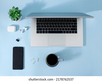 Creative Office Environment And Working Atmosphere For Working At Home. Coffee, Laptop, Phone And Headphones On Pastel Blue Desk Background.