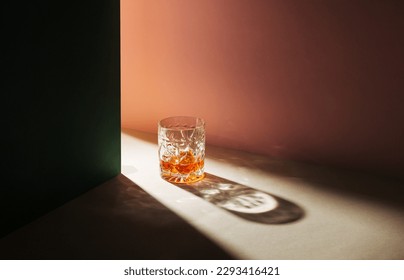 Creative party concept crystal glass with whisky. Minimal scene strong drink on beige, pink and green background.