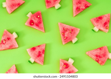Creative pattern composition with Christmas trees made of fresh watermelon slices on green background. Minimal Christmas or New Year concept. Trendy holiday fruit backdrop idea. Flat lay.