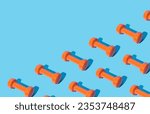 Creative pattern composition made of orange dumbbells on light blue background with copy space. Minimal fitness, healthy lifestyle and sport concept. Trendy exercise and fitness background idea.